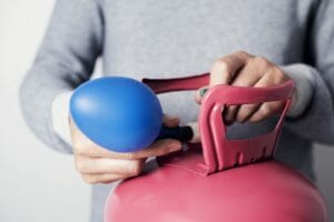 Ballongas wird von männlichen Händen von Gasflasche in Luftballon gefüllt