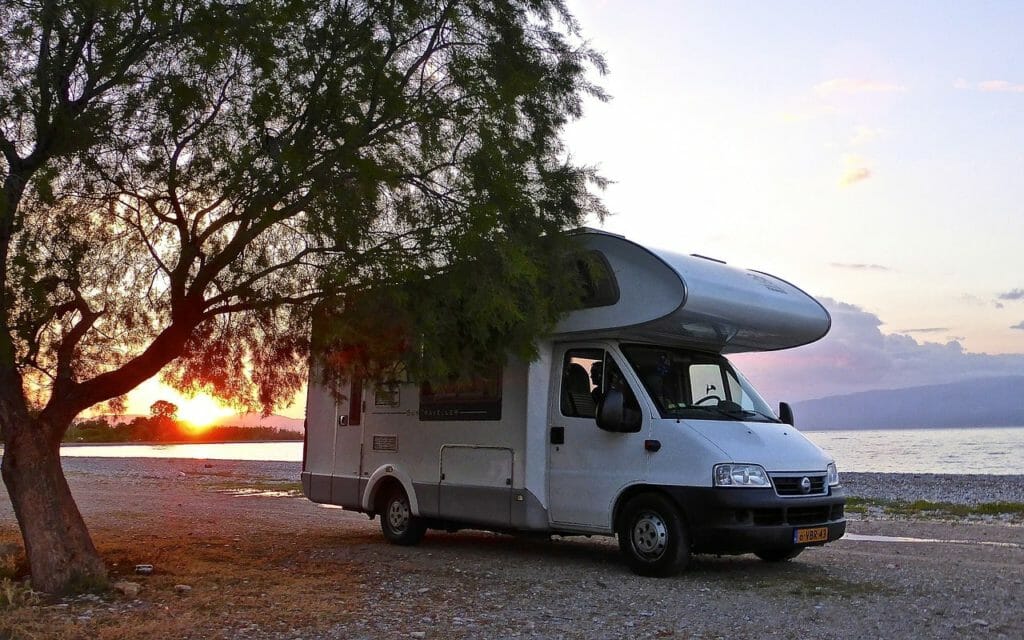 Wohnmobil steht neben einem Baum an einem Strand 