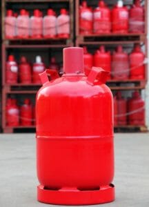 Rote Pfandgasflasche auf einem Hof mit Gasflaschenlager im Hintergrund