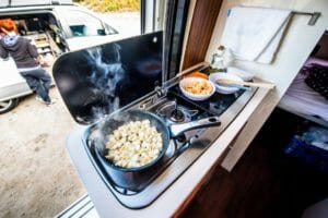 An Flaschengas Gasflasche angeschlossener Campingkocher in Wohnmobil mit Pfanne auf Gasherd und offener Tür