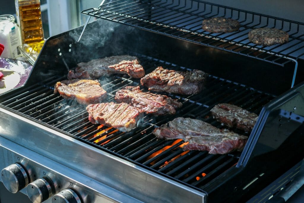 Gasflaschen Gasgrill mit mehreren Brennern bei sonnigem Wetter mit Fleisch auf dem Rost