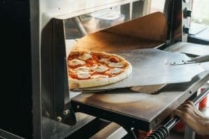 Pizzabäcker holt Pizza aus Gas Pizzaofen, der mit Propan betrieben wird