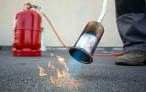 Rote Flaschengas Gasflasche beim Dachdecker, Brenner erwärmt mit Flamme die Dachpappe