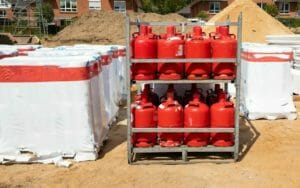 Zwei Paletten rote Gasflaschen für Gewerbe stehen übereinander zwischen Baumaterial auf Baustelle