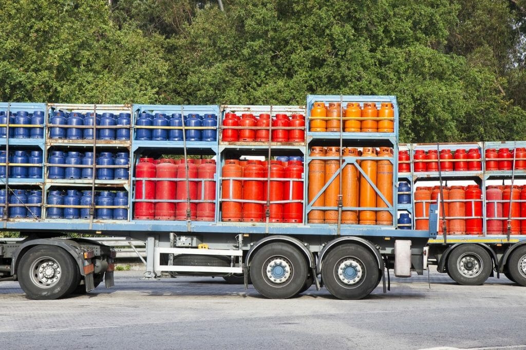 Verschieden farbige Gasflaschen stehen in Transportkäfigen auf einem Trailer im Hof zum Gasflaschen Transport