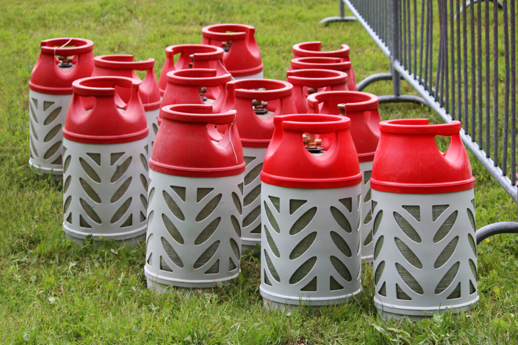 Composite gas cylinders of red and gray color in volume of 18,2 liters stand on a grass in city park